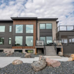 beautiful modern home here pictured is the back featuring a lot of large windows in black brown frames.